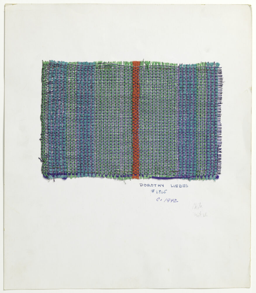 woven textile sample of varying blue threads with a coral thread in the middle of the sample, mounted onto a white board