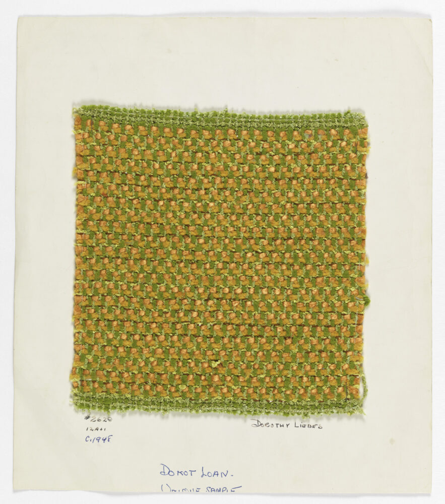 woven textile sample of orange and green threads mounted onto a white board