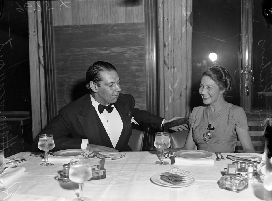 black and white image of a man and woman in formalwear sitting at a dining table.