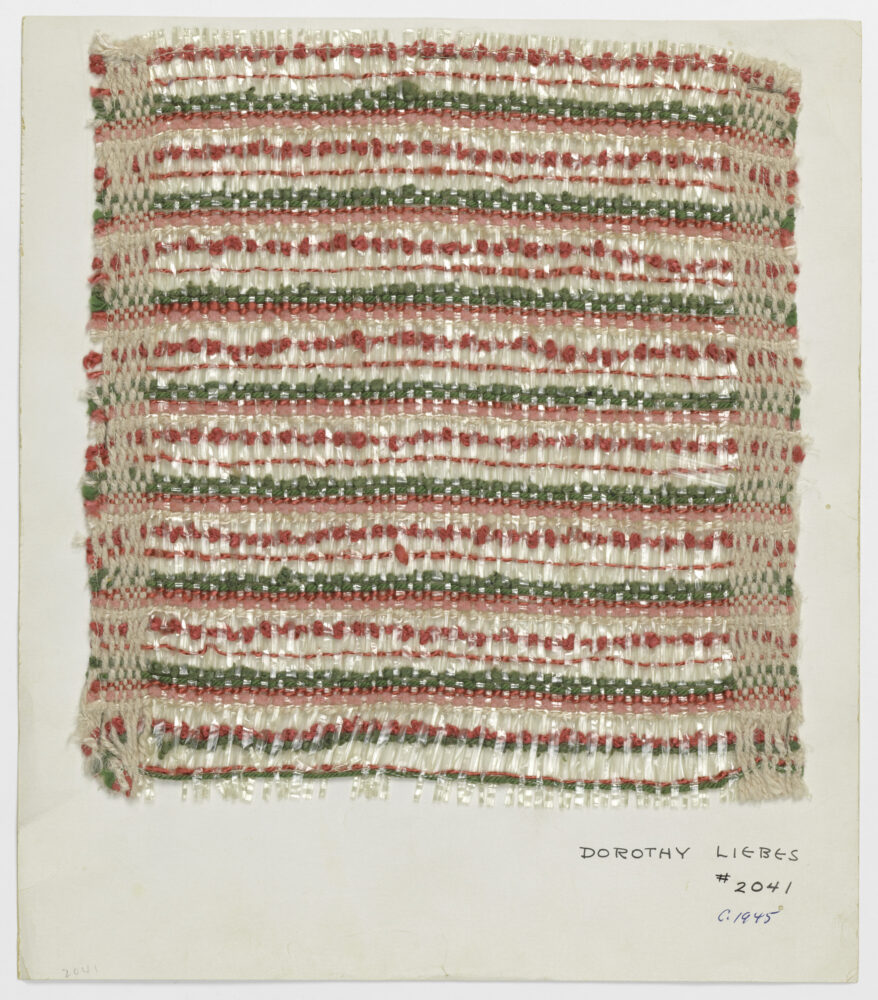 red, green, and clear threads woven into a striped sample mounted onto white board