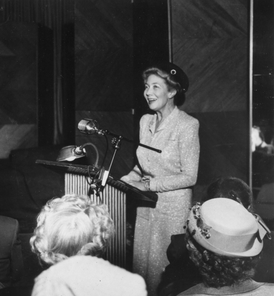black and white photograph of a woman wearing a sparkly suit standing at a podium in front of a crowd