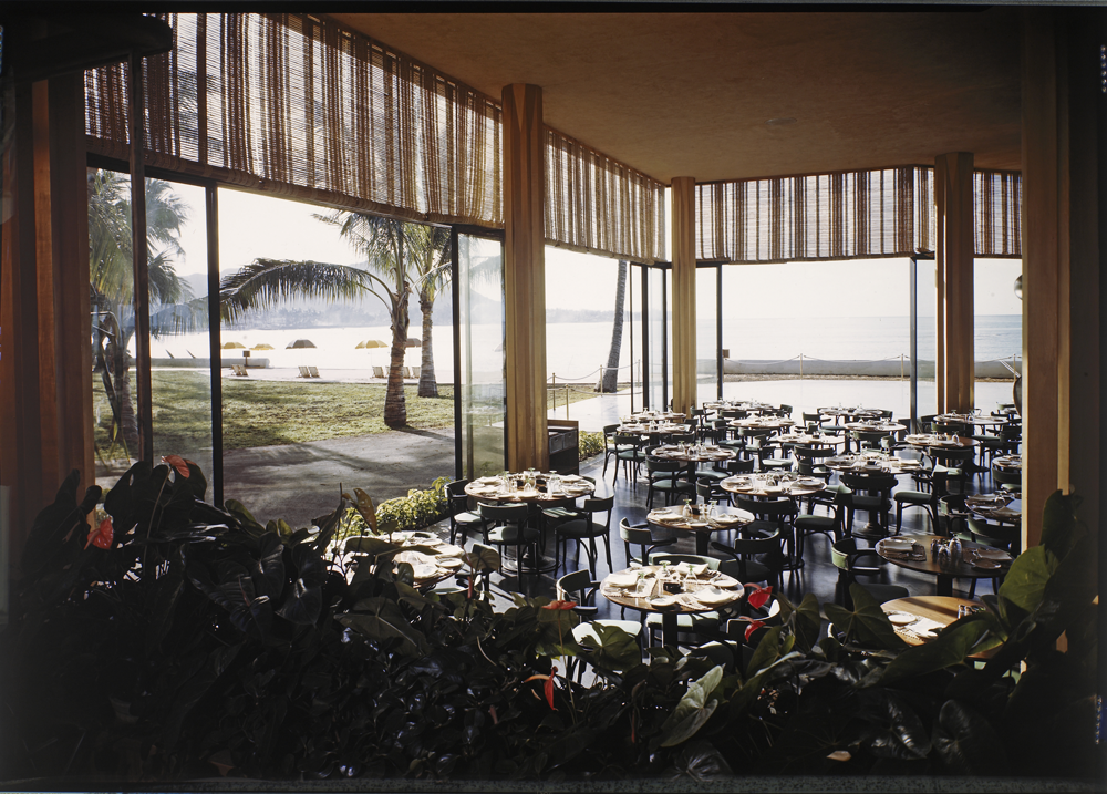 color image of a restaurant with open walls and large columns, at the top of the windows there are window blinds