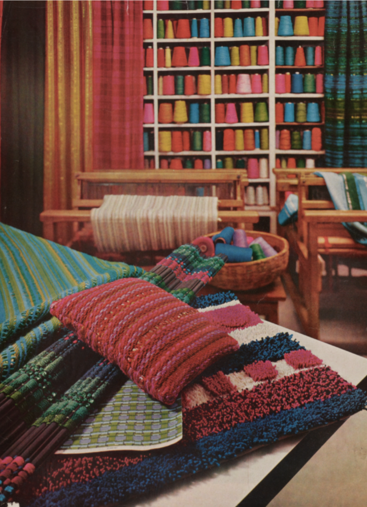 Color photograph of a room with shelves filled with colorful spools of yarn, fabrics, carpet samples, and pillows.