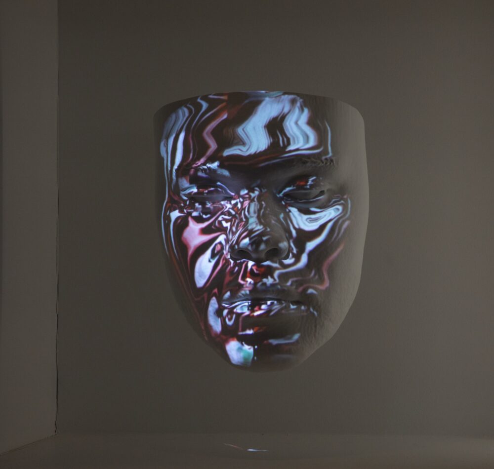 White model of a face suspended in air; blue and pink wavy lines are projected onto the surface of the face.