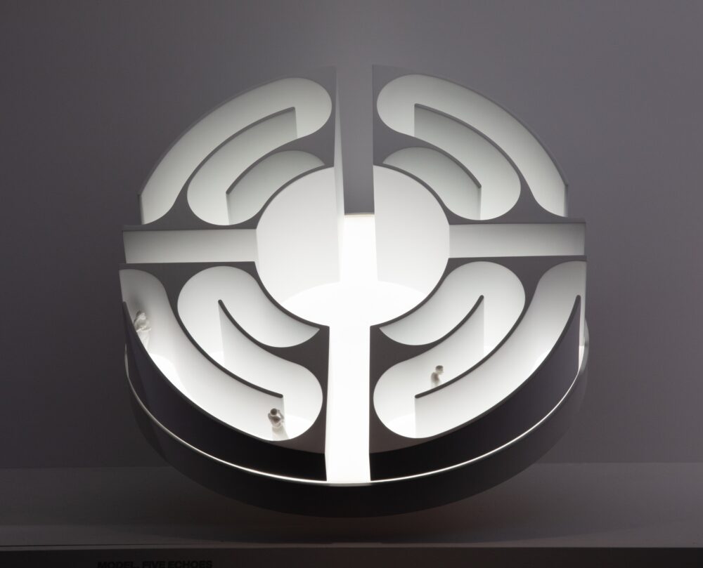 White model of a circular structure with a winding path in each quadrant. White light is glowing from within the model.