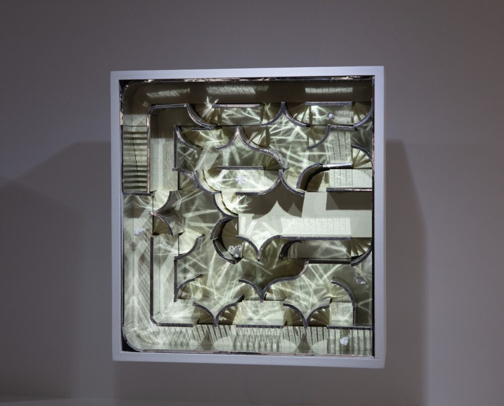Model of a top-view plan for an interior space faces the viewer; it has winding paths, curved lines, and several staircases. White light is reflected throughout the model making many faded lines of light.