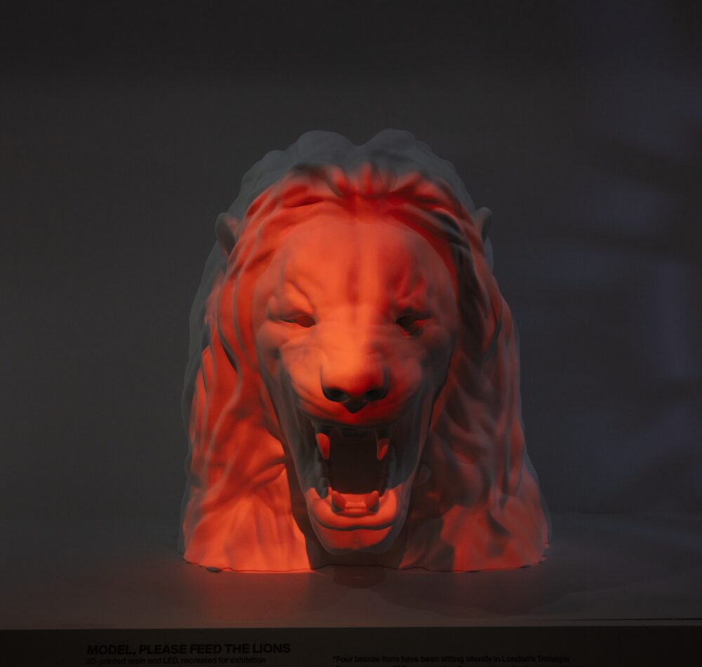 Straightforward view of a white model of a roaring lion’s head with red light projected on top.