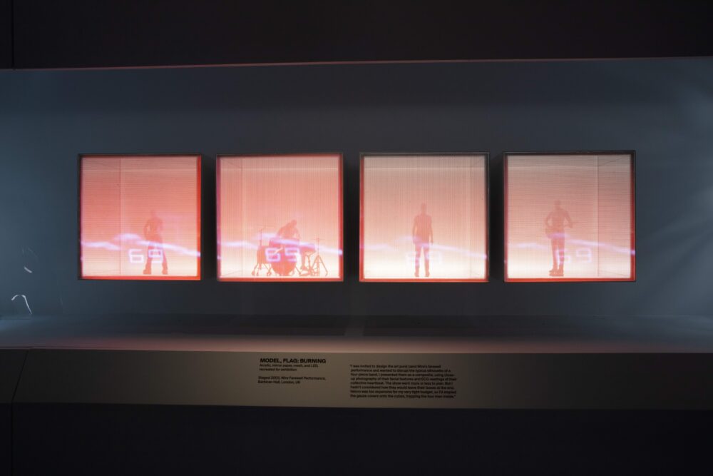 Installation view of a model comprising four red-lit cubes lined up next to each other. Inside each cube is a figure playing an instrument.