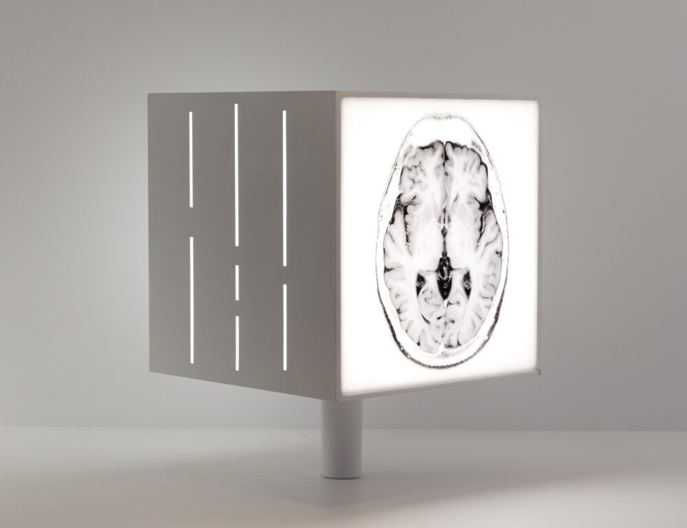 White cube model emitting white light; two sides are shown: one with several vertical line cutouts and the other of a brain scan.