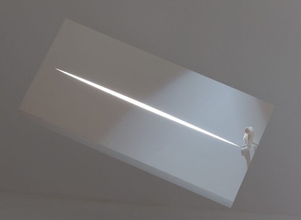 Top view of a white model of a small figure at the base of a rectangle with a long fissure running along the middle from which white light glows.