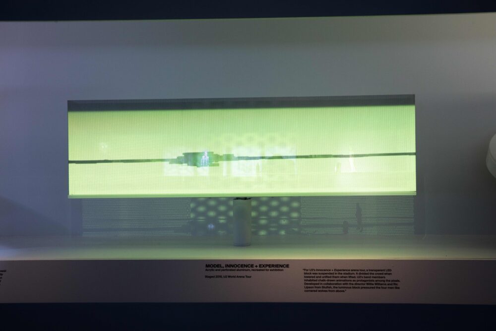 Installation view of a horizontal, rectangular model emitting green light; a black horizontal line cuts the rectangle in half.