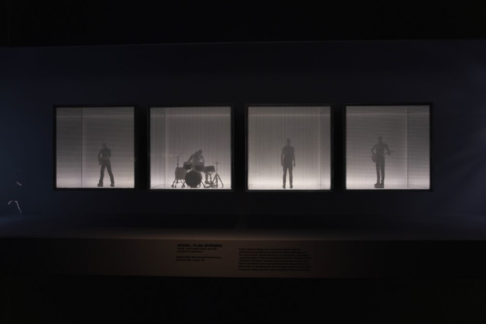 Installation view of a model comprising four cubes lined up next to each other. Inside each cube is a figure playing an instrument.