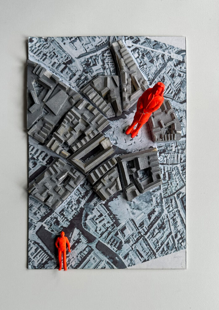 A blue and gray rectangular model of the top view of a city. Two red figures are included: one is at the bottom left corner and the other stands towards the top right.