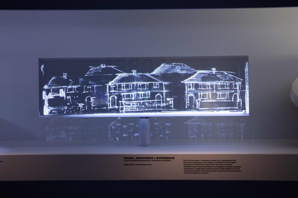 Installation view of a horizontal, rectangular model emitting white light; a black-and-white illustration of houses is projected on the surface.