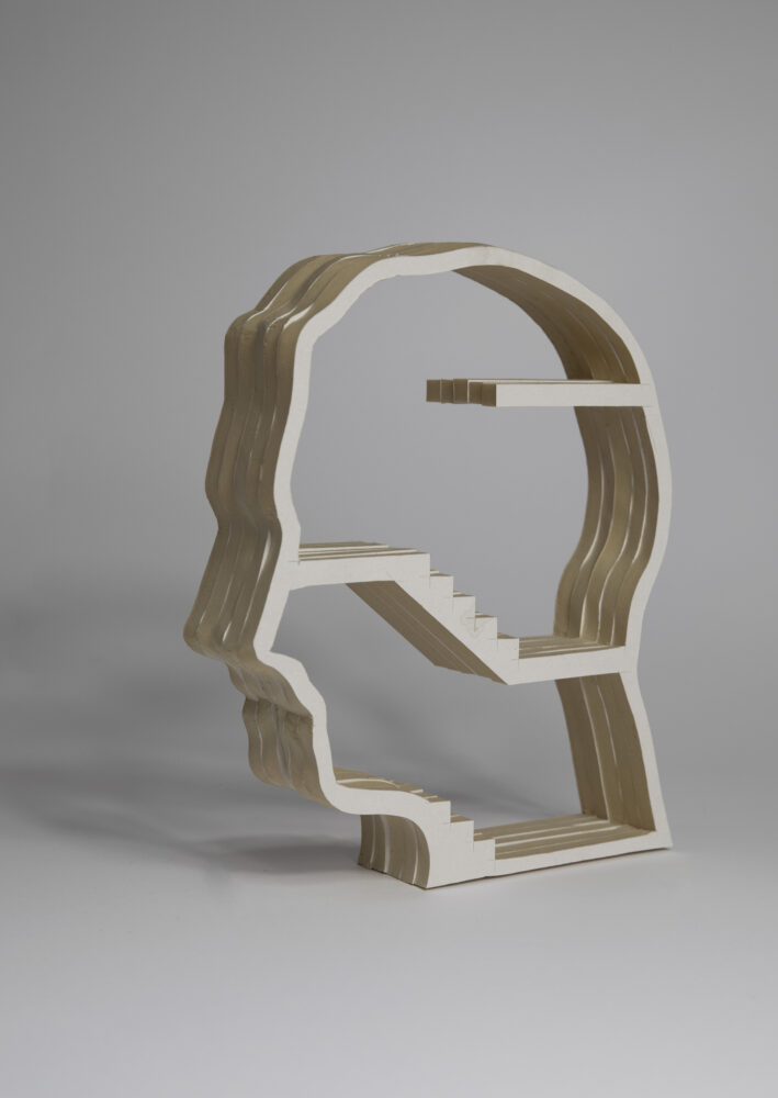Sculpture of the outline of a head in profile, facing left, made of layers of a white material. Within the main structure are two sets of stairs and several platforms dividing the space in three sections.