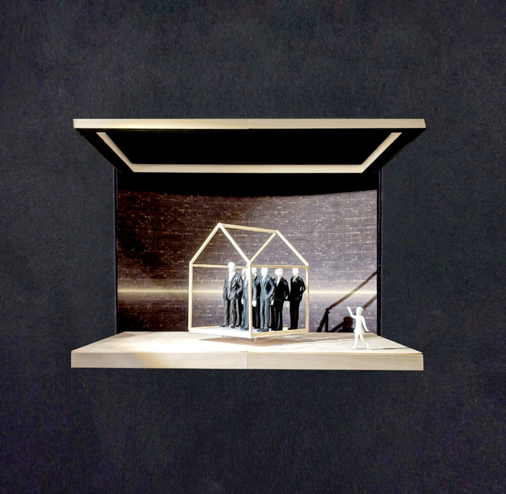Model for a stage design with a basic structure in the shape of a house on the stage, within which a group of figures in suits are standing. The dark backdrop is cut horizontally by a line of white light.