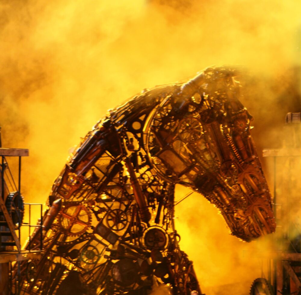 Profile view of a complex sculpture of a horse head made of small machine pieces put together with spaces between them, allowing the viewer to see through the horse. It is surrounded by a yellowish haze.