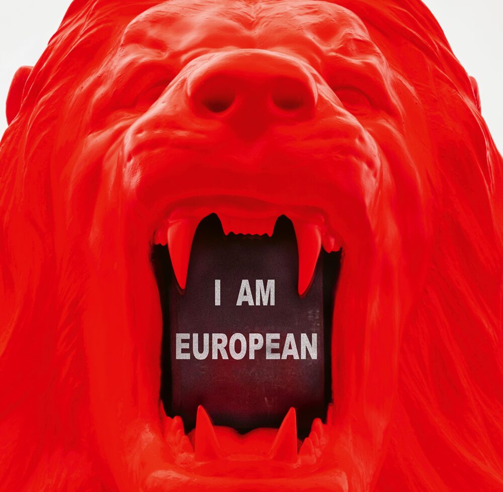 Zoomed-in view of a red model of a roaring lion’s head; inside its mouth is a screen that reads “I AM EUROPEAN” in uppercase letters.