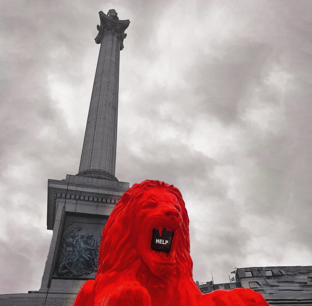 Upward view of a red model of a roaring lion’s head in front of a black and white image of a city landmark; inside its mouth is a screen that reads “HELP” in uppercase letters.