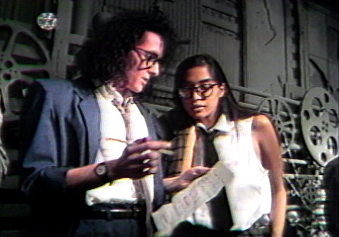 Image of two models, male and female, dressed in WilliWear business attire, wearing glasses, and reading notes on a sheet of paper