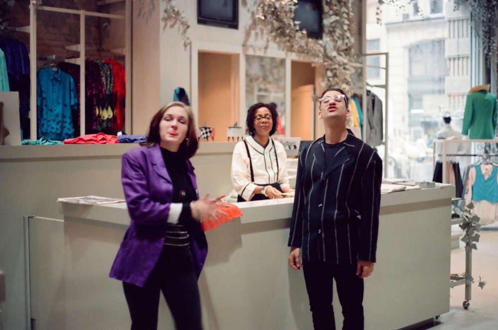 Two young women and one young man make "funny faces" at the camera while standing at the front desk of a clothing store.