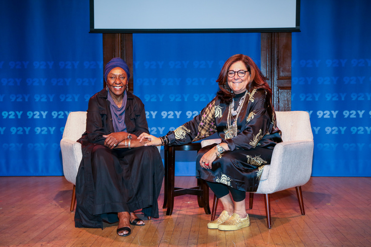 Two women sit together smiling on a stage.