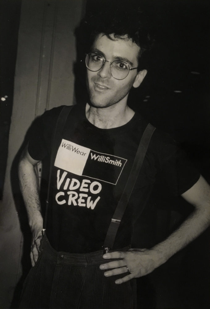Grayscale image of man wearing corduroy overalls and black T-shirt with text stating, “WilliWear Willi Smith Video Crew”