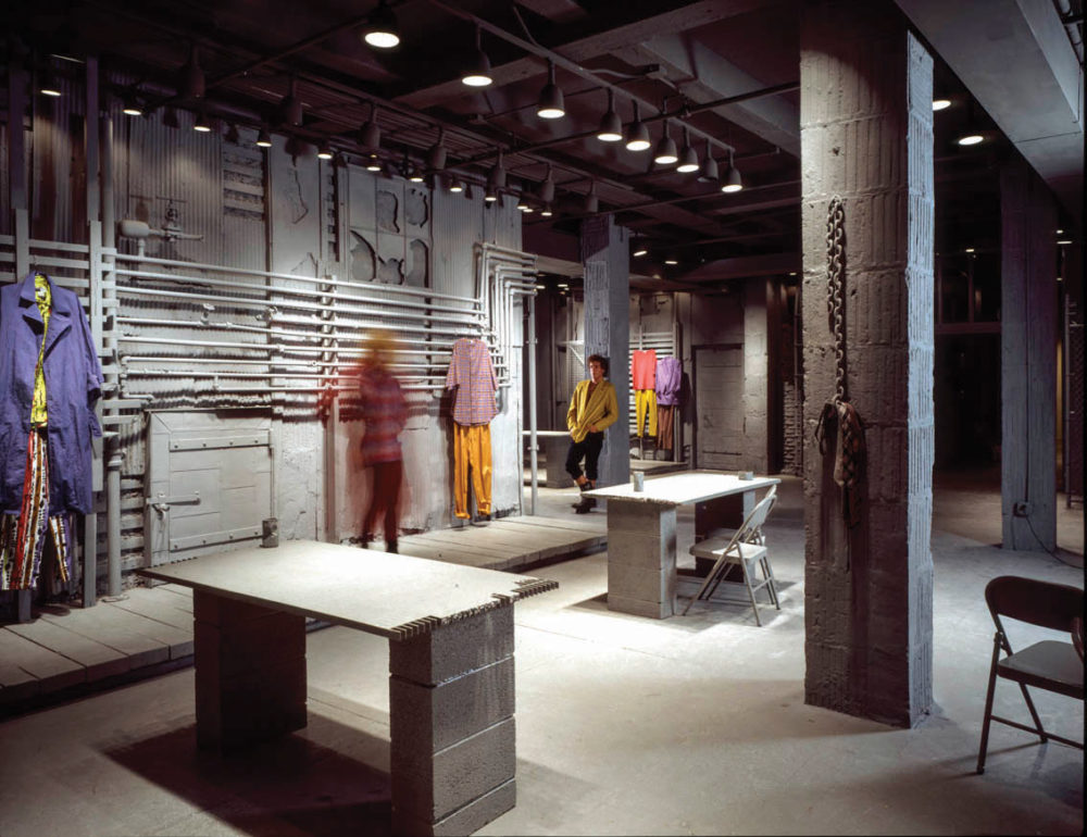 Image of brightly colored clothing hanging from gray pipes and worn by two models in WilliWear New York showroom