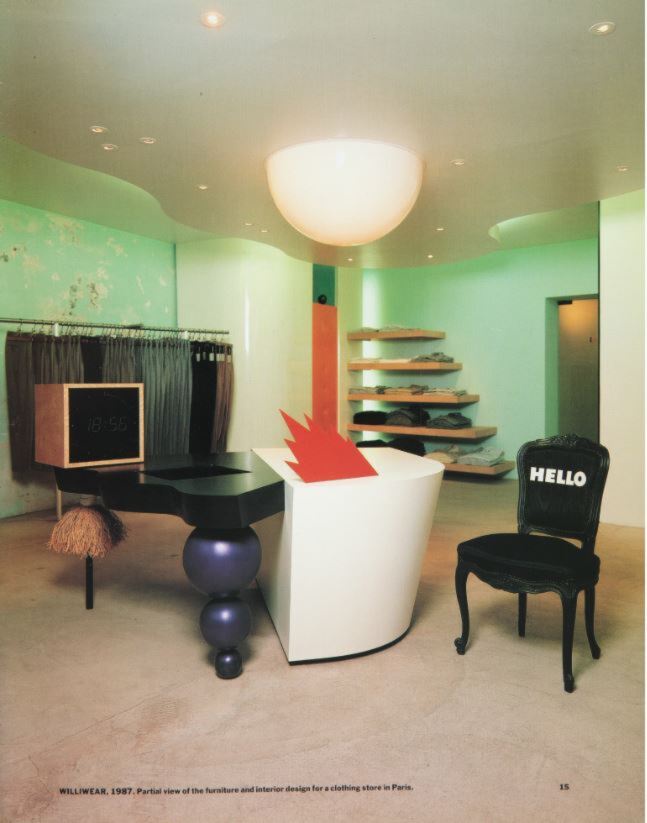 A room with light green walls, filled with abstract furniture and wooden shelves stacked with clothing