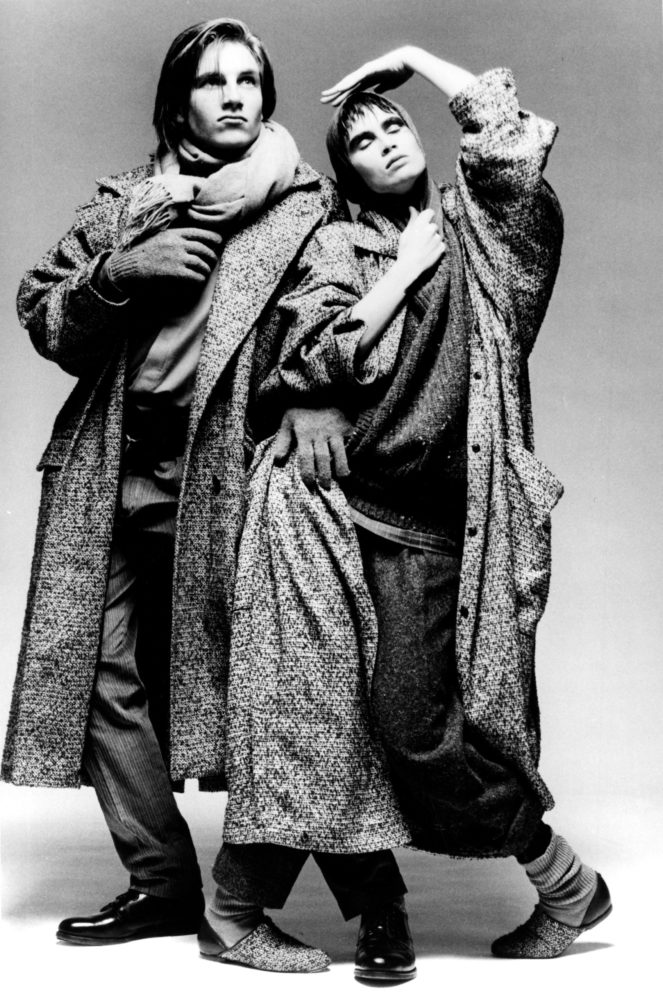 Grayscale image of two figures posing dramatically in matching oversized trench coats